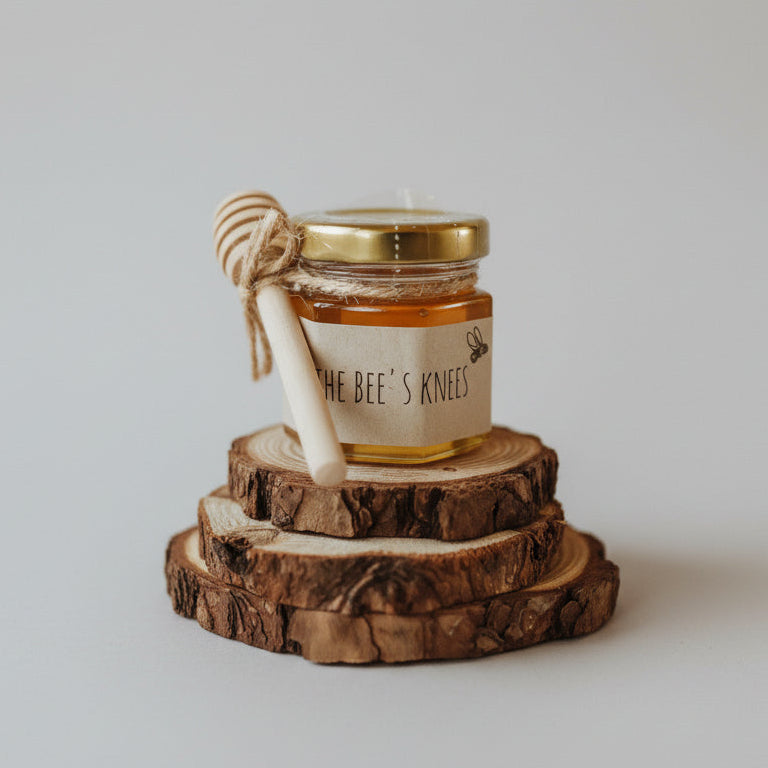 Jar of honey labeled 'The Bee's Knees' with a honey dipper on a wooden surface, blurred lights in the background