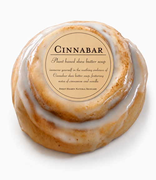 A round bar of Cinnabar Shea Butter Soap styled like a cinnamon roll with white icing, featuring a circular label on top with the brand name 'Cinnabar' and scent notes of cinnamon and vanilla.