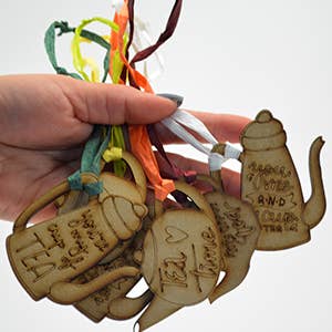 Wooden tea-themed keychains with decorative ribbons held by a hand on a white background